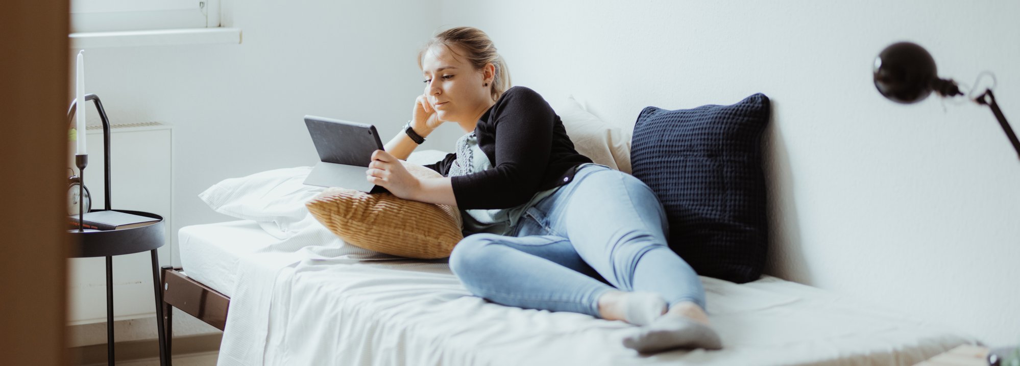 Junge Frau, die auf dem Bett liegt und auf den Bildschirm eines Tablets blickt.