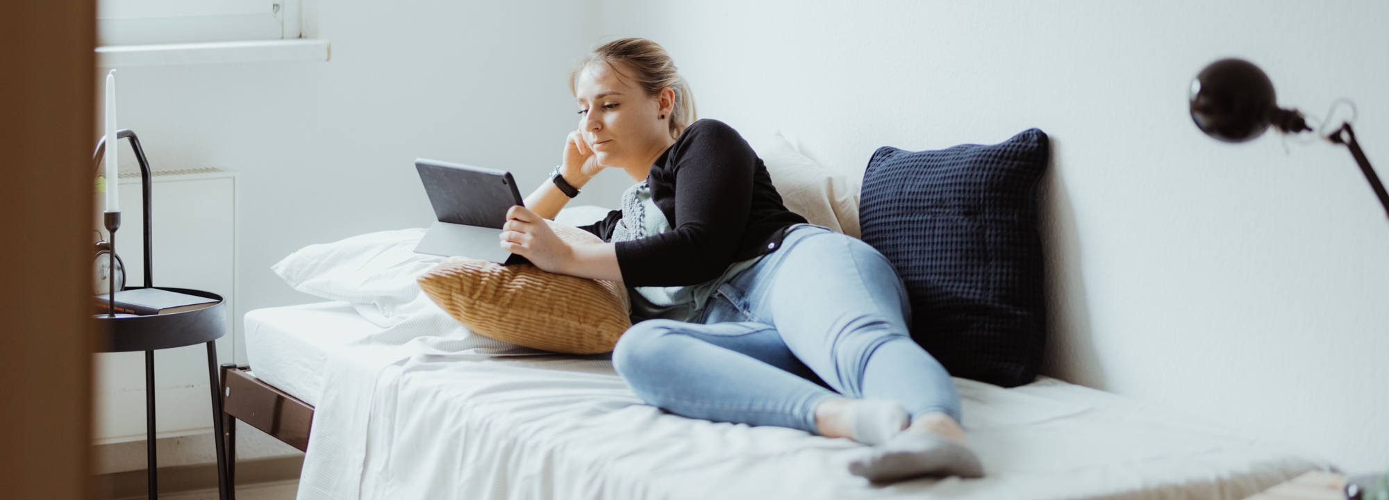 Junge Frau, die auf dem Bett liegt und auf den Bildschirm eines Tablets blickt.